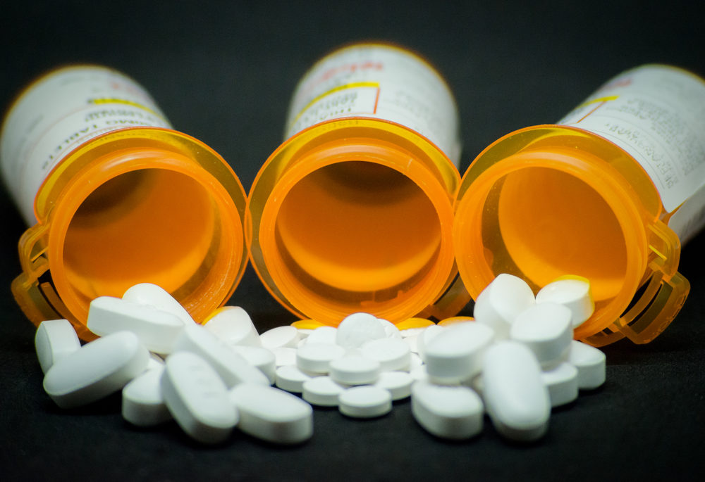 White pills spill from three overturned prescription bottles