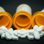 White pills spill from three overturned prescription bottles