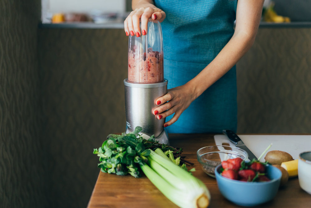 woman blending a smoothie at a counter with fruits and vegetables