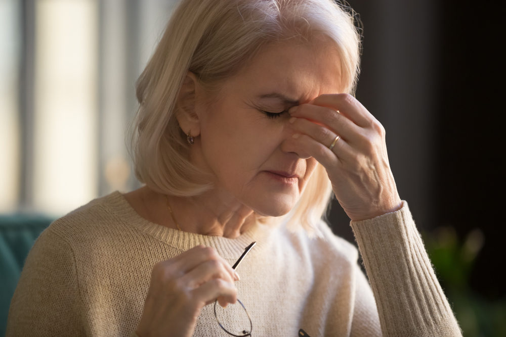 An older woman removes her glasses to massage her eyes