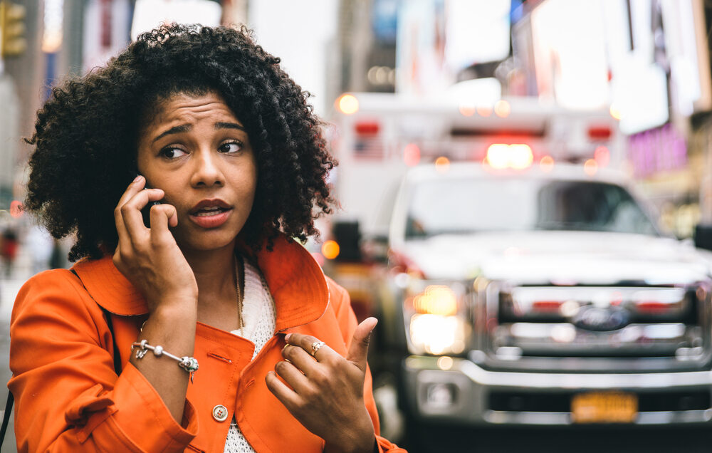 afro american woman calling 911 after a car accident with ambulance in background