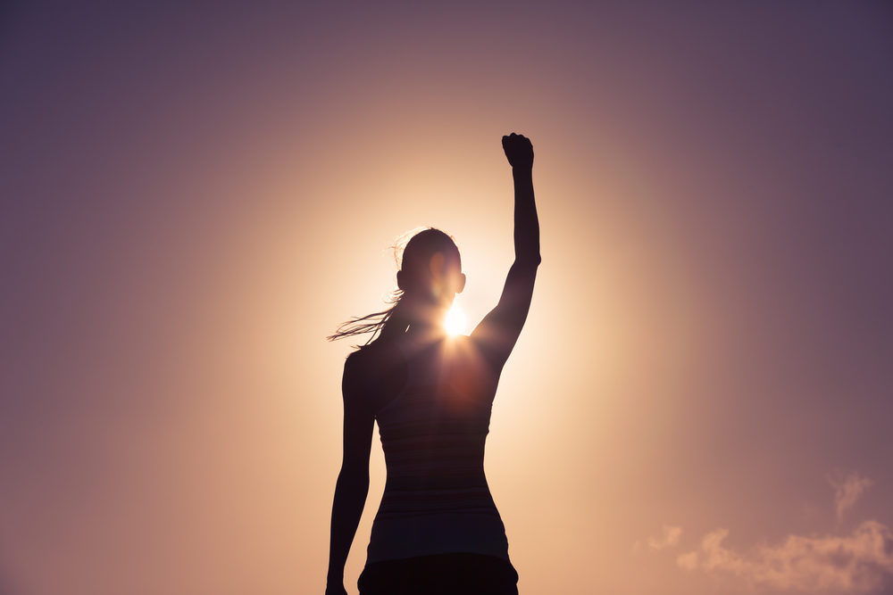 Silhouette of a woman against a sunset with her fist pumped in the air