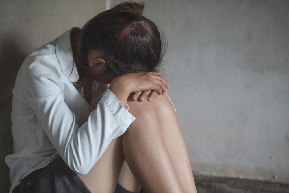 A woman sits on the floor with her head on her knees