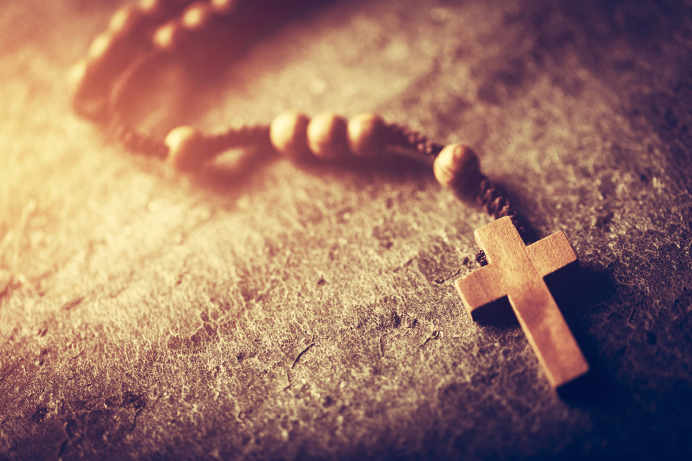 wooden rosary with cross on stone with light shining upon it