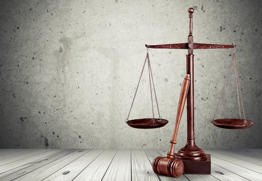 Mass Torts vs Class Action Lawsuits wooden scales of justice with a gavel leaning against them on a white-washed wood background