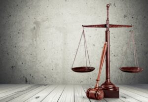 wooden scales of justice with a gavel leaning against them on a white-washed wood background