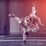 Two strong wrestlers in blue and red wrestling tights are wrestlng and making a making a hip throw on a wrestling carpet in the gym.