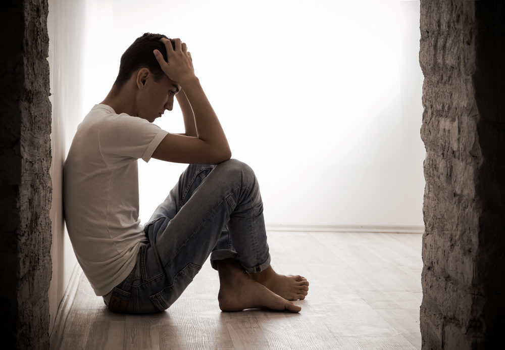 A distraught looking young man sits on the floor against a wall