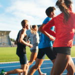 Rear view of young people running together on race track.
