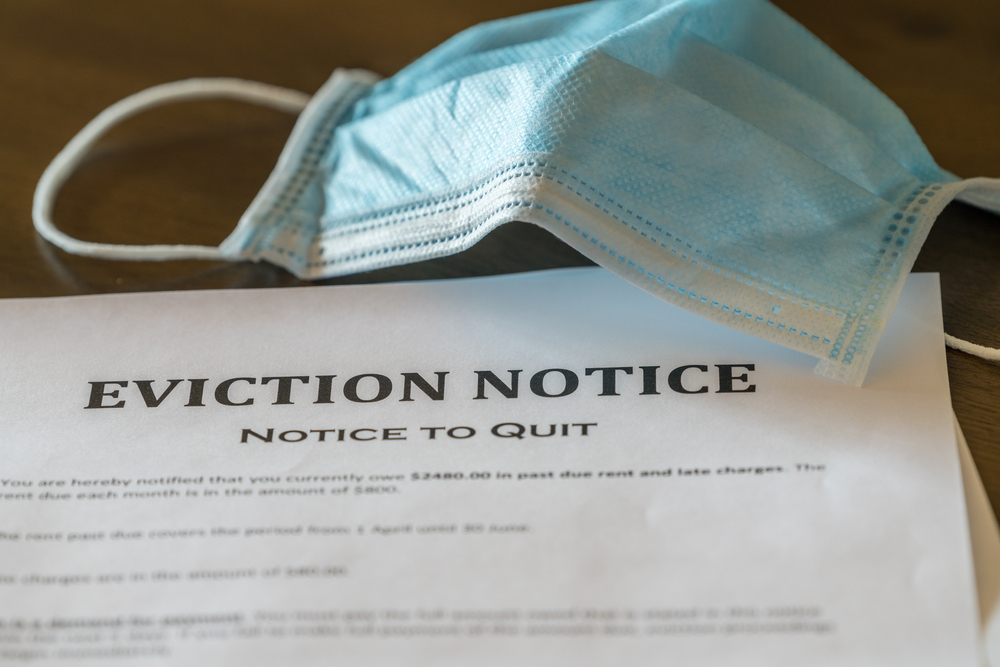 Defaulting renter with facemask receives letter giving notice of eviction from home on wooden table