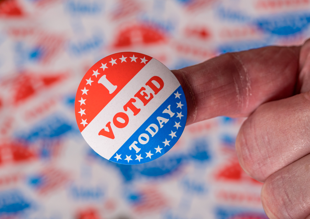 Finger with I Voted Today button in front of many voting stickers given to US voters in Presidential election