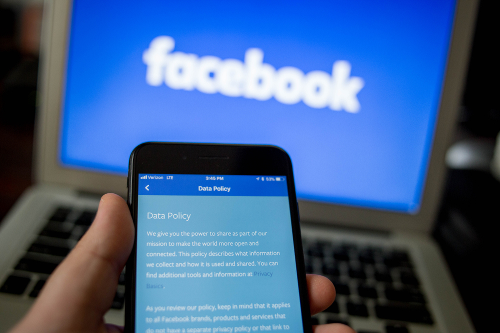 a screen from the Facebook app is seen on an iPhone in front of a Facebook logo