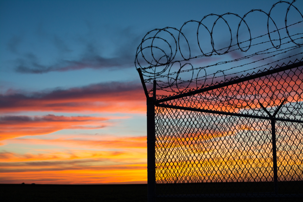 Dramatic sunset with chain link fence and razor wire silhouette.