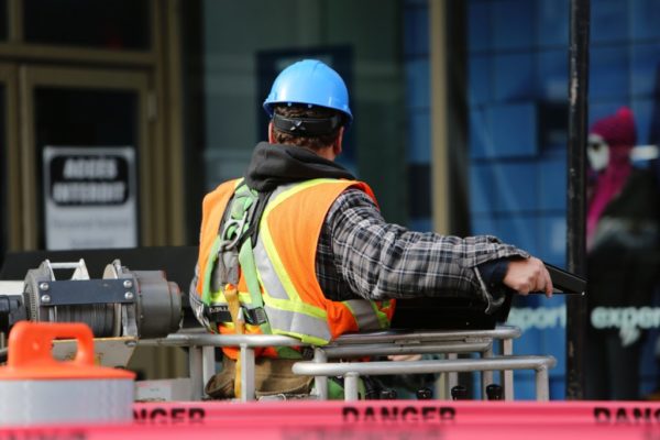 A construction worker at a job site wearing an orange safety vest and blue hard hat