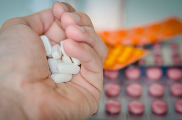 A handful of white tablet pills with blister packs of medication in the background