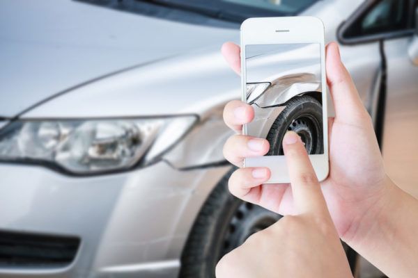 A car accident victim takes a photo of her damaged vehicle using a smartphone