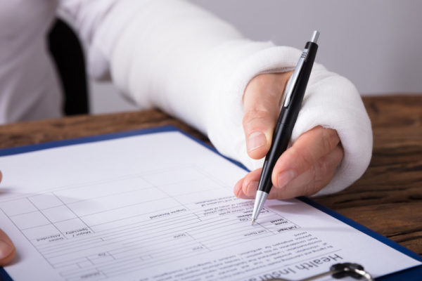 A man with his forearm in a cast filling out a health insurance form