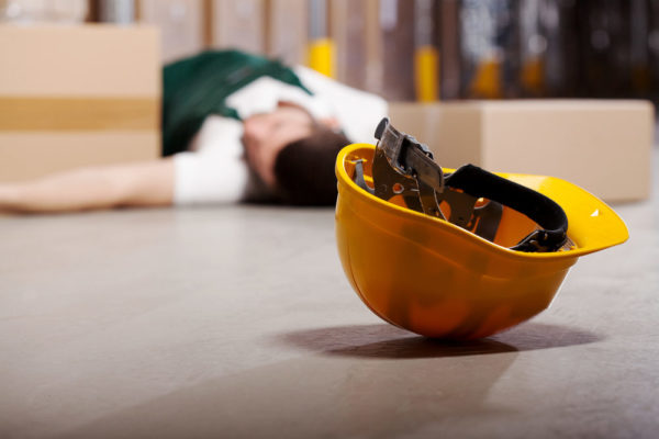 An injured worker lies on the ground, his dislodged safety helmet in the foreground