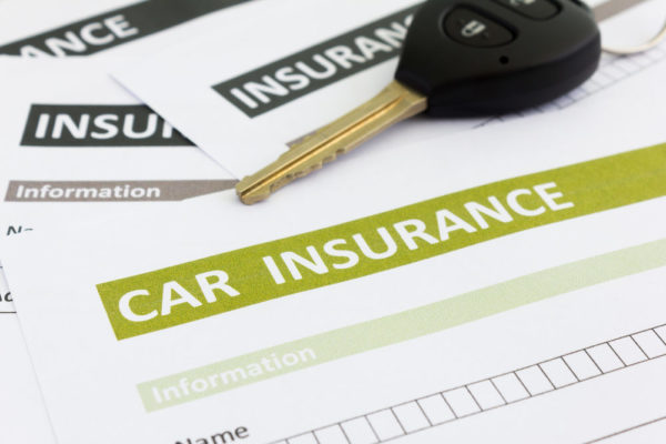 A set of car keys rests on top of a pile of auto insurance forms