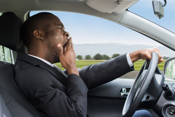 A businessman yawns while driving a speeding car through the countryside