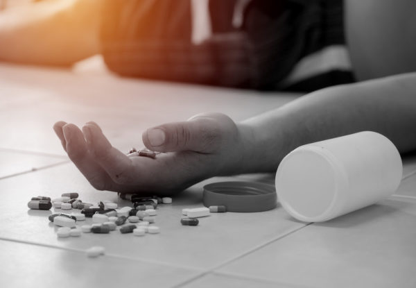 A hand full of pills spilling on to the floor, the owner unconscious from an apparent drug reaction