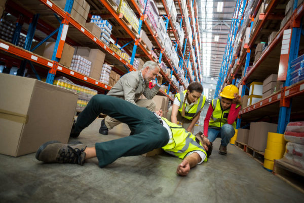 Workers tending to an injured employee sprawled on a warehouse floor