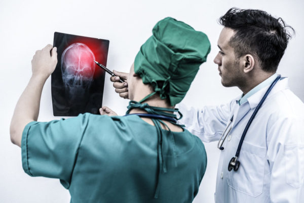 A doctor and a surgeon look over a head x-ray with obvious brain trauma