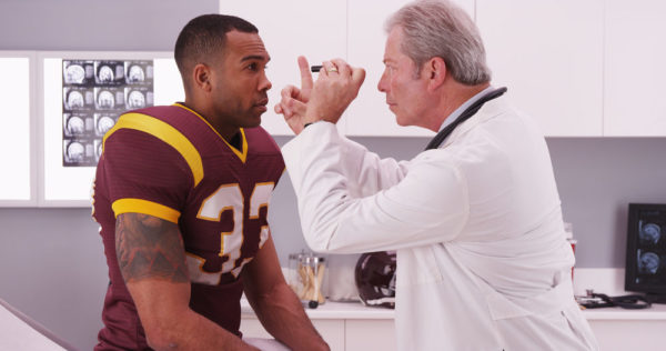 A doctor checks a football player for mild brain injury symptoms by tracking the athlete's eye movement using his finger
