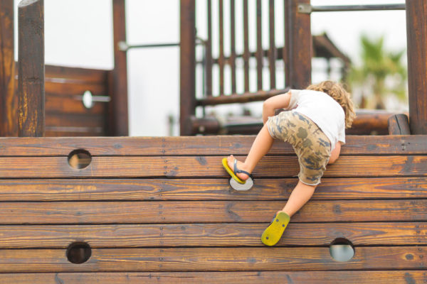 A young child climbing a potentially dangerous wooden structure at a playground