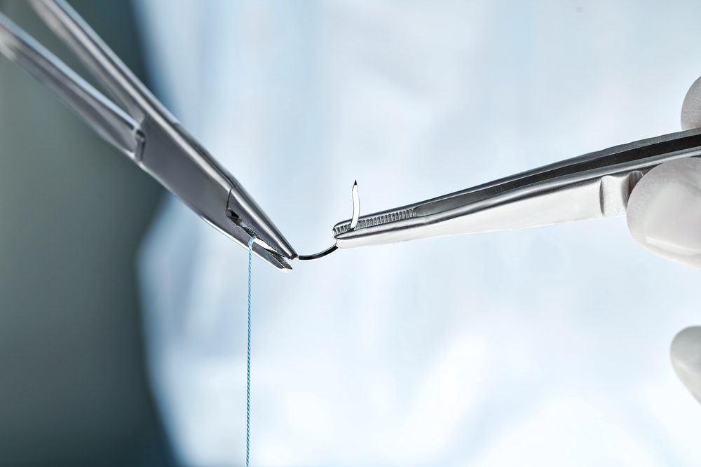 Close up of surgeon holding needle holder and suture material.