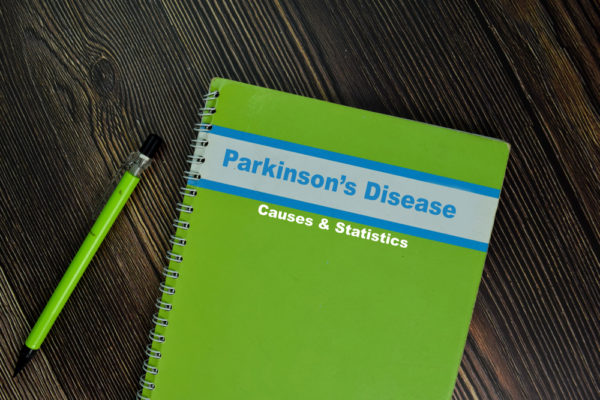 Notebook of Parkinson's Disease Causes and Statistics isolated on Wooden Table.