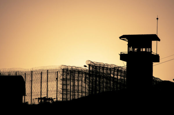 Silhouette of barbed wires and watchtower of prison at sunset