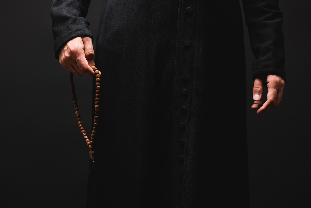 partial view of priest holding rosary beads in hand isolated on black