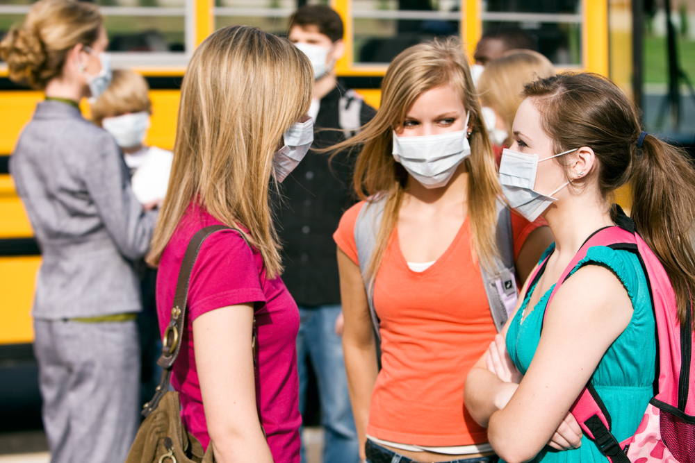 Students near a school bus wearing medical masks.
