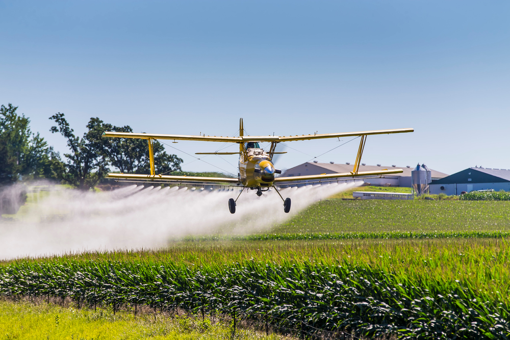 A crop duster applies chemicals to a field of vegetation.