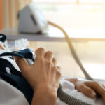 Close up of senior patient woman hand holding Cpap mask between the chest lying in hospital room.