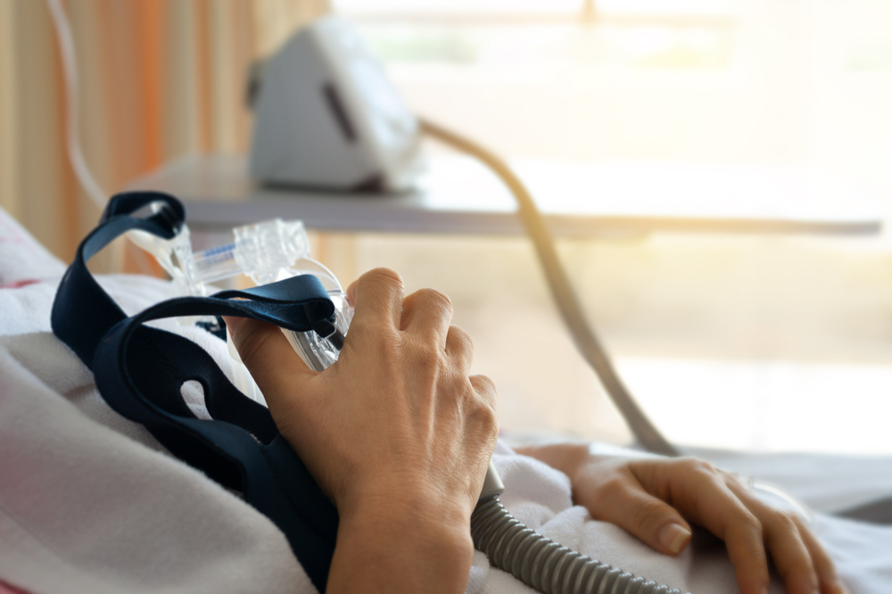 Close up of senior patient woman hand holding Cpap mask between the chest lying in hospital room.