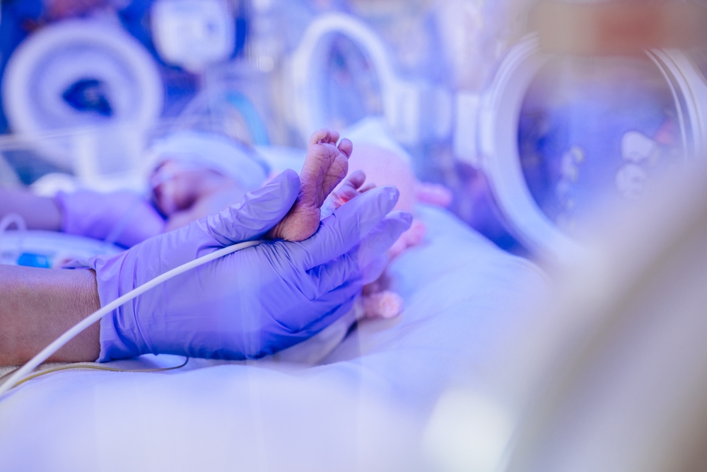 Macro photo of doctor's hands and legs of a child. Newborn is placed in a medical incubator under ultraviolet lamp.