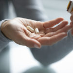 Close up of young female hands holding opened pill bottle and two soft-shelled capsules