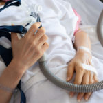 Senior patient woman hand holding Cpap mask between the chest lying in hospital room.