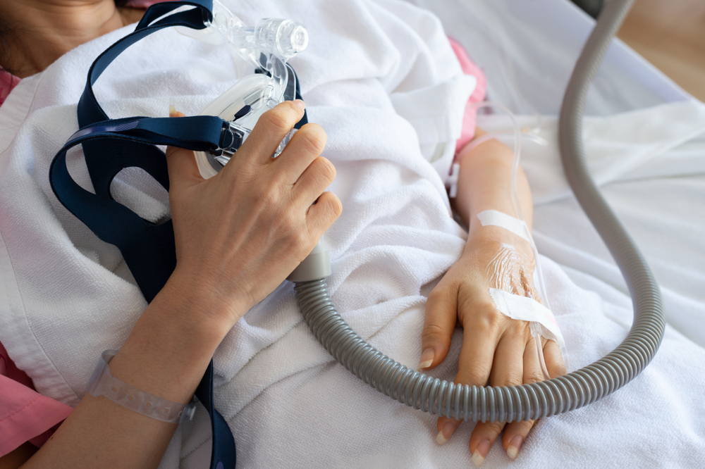Senior patient woman hand holding Cpap mask between the chest lying in hospital room.