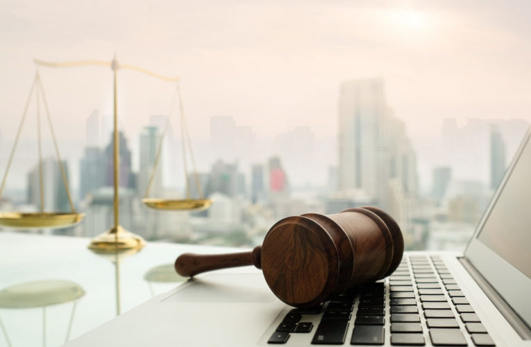 Gavel resting on laptop at desk with scales of justice behind city view background