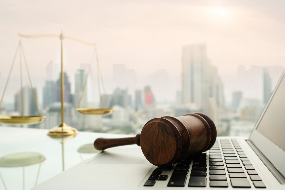 Gavel resting on laptop at desk with scales of justice behind city view background