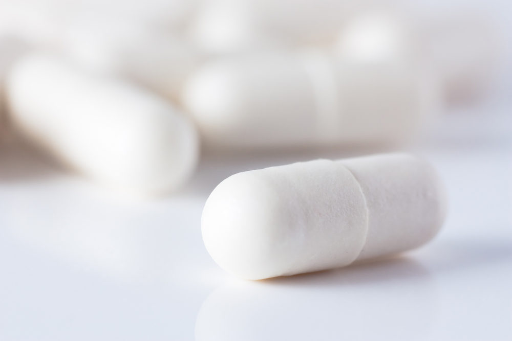 $Macro shot of white capsuled pill and a heap of same pills on background