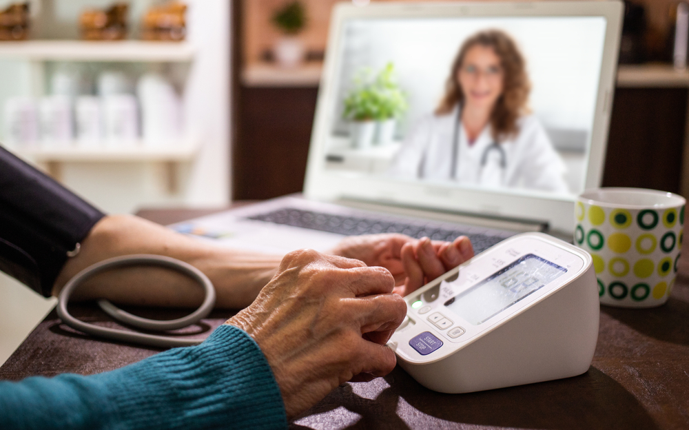 telemedicine concept elderly woman speaking to her doctor online and taking her blood pressure