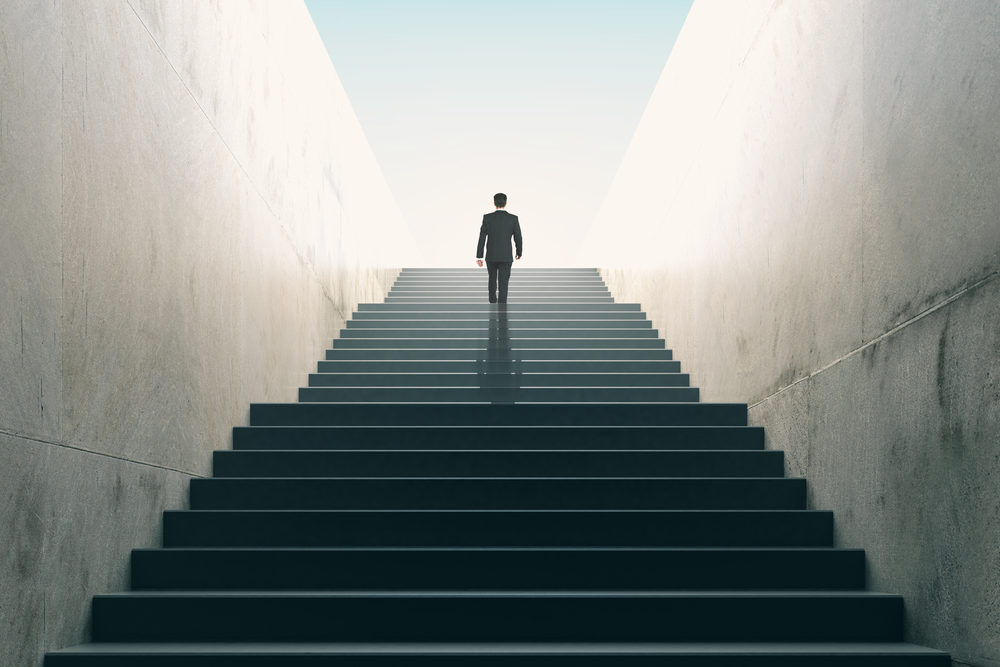 A man reaches the top of a tall non-descript staircase
