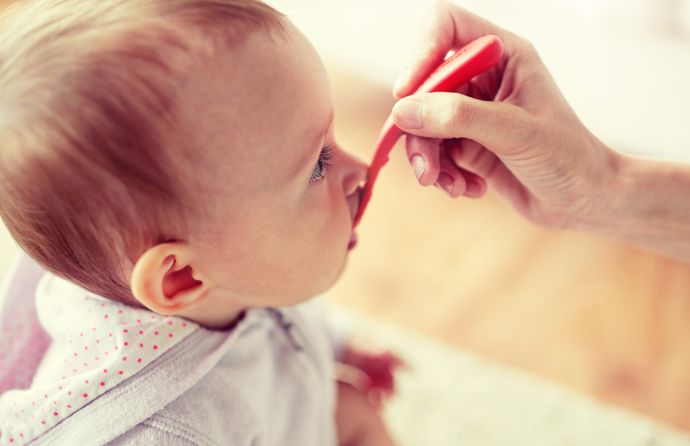 close up of hand with spoon feeding little baby at home