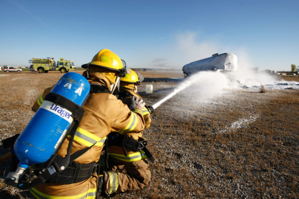firefighters spray foam to put out a simulated fire and crash of an airplane during a disaster drill