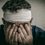 man holding his face with a bandaged head injury