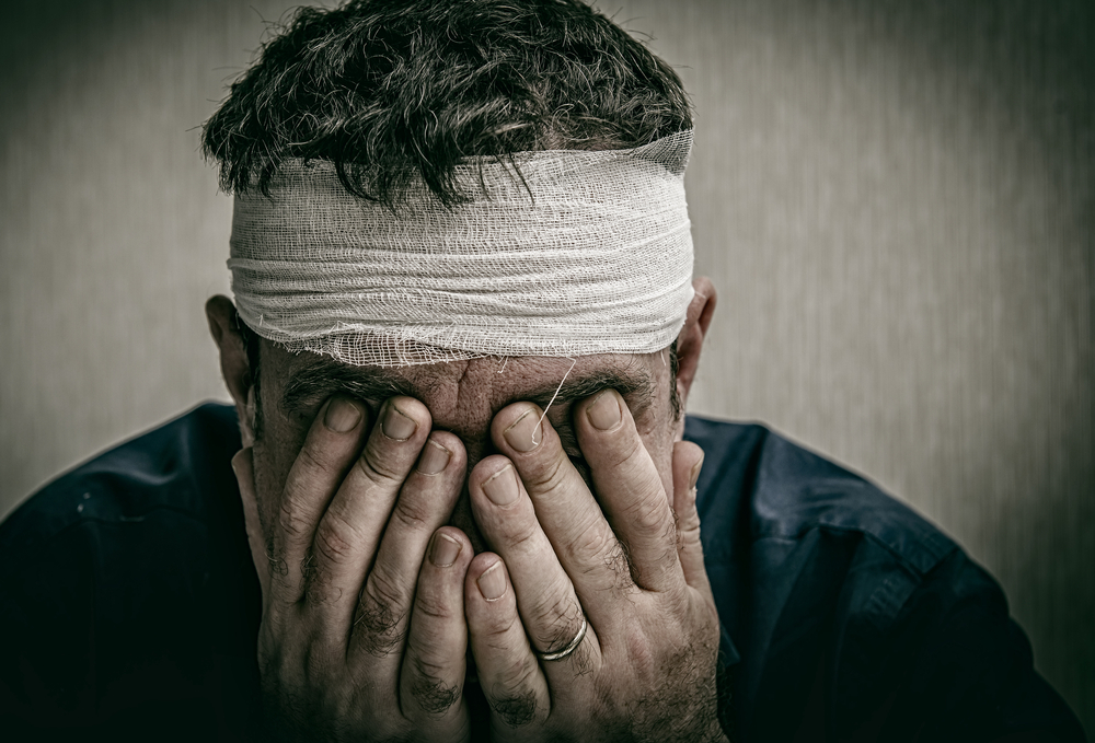 man holding his face with a bandaged head injury